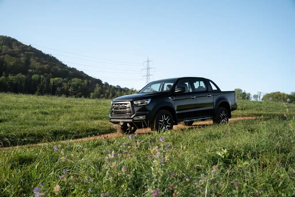 Pick-up JAC T8 essence noir de profil roulant sur une rouet de campagne sur fond de ciel bleu
