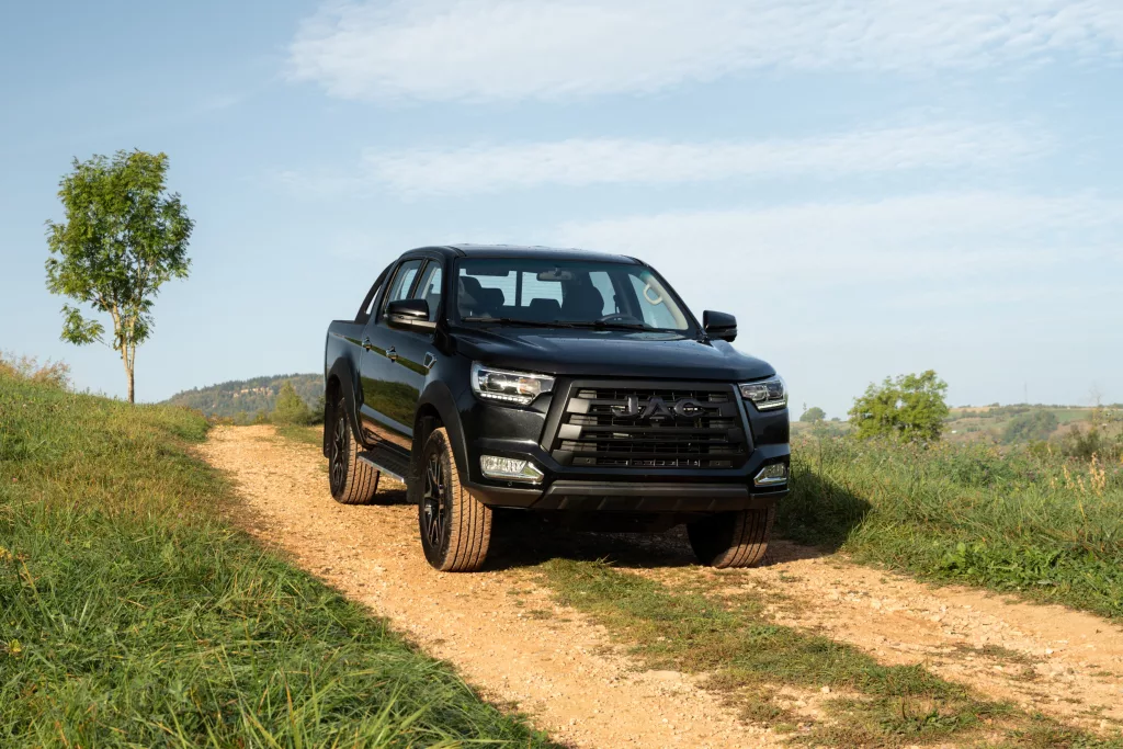 JAC T8Pro essence noir de profil roulant sur route de campagne avec de l'herbe verte et du ciel bleu